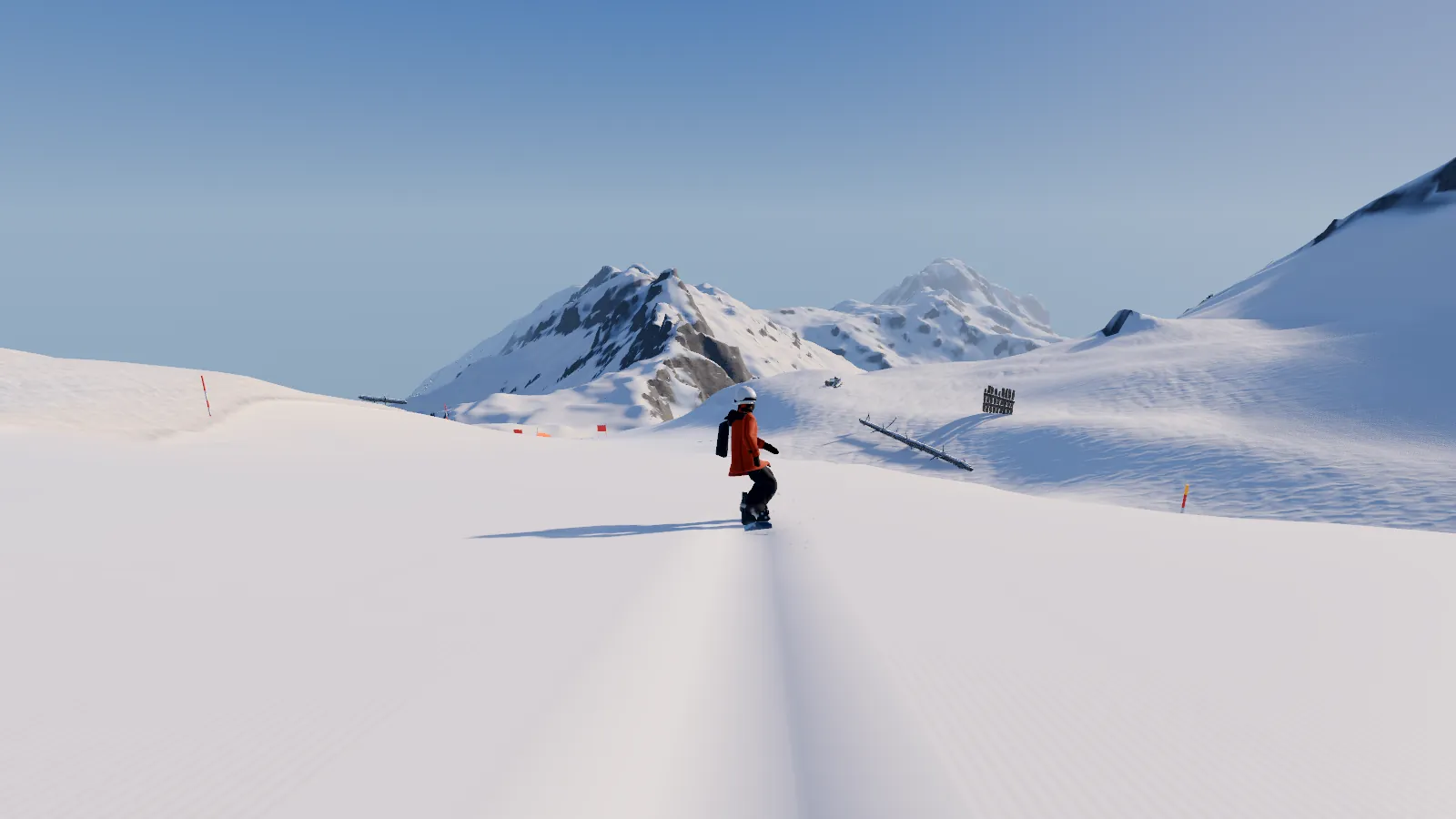 A rider in an orange jacket drops onto open snow below a rocky summit